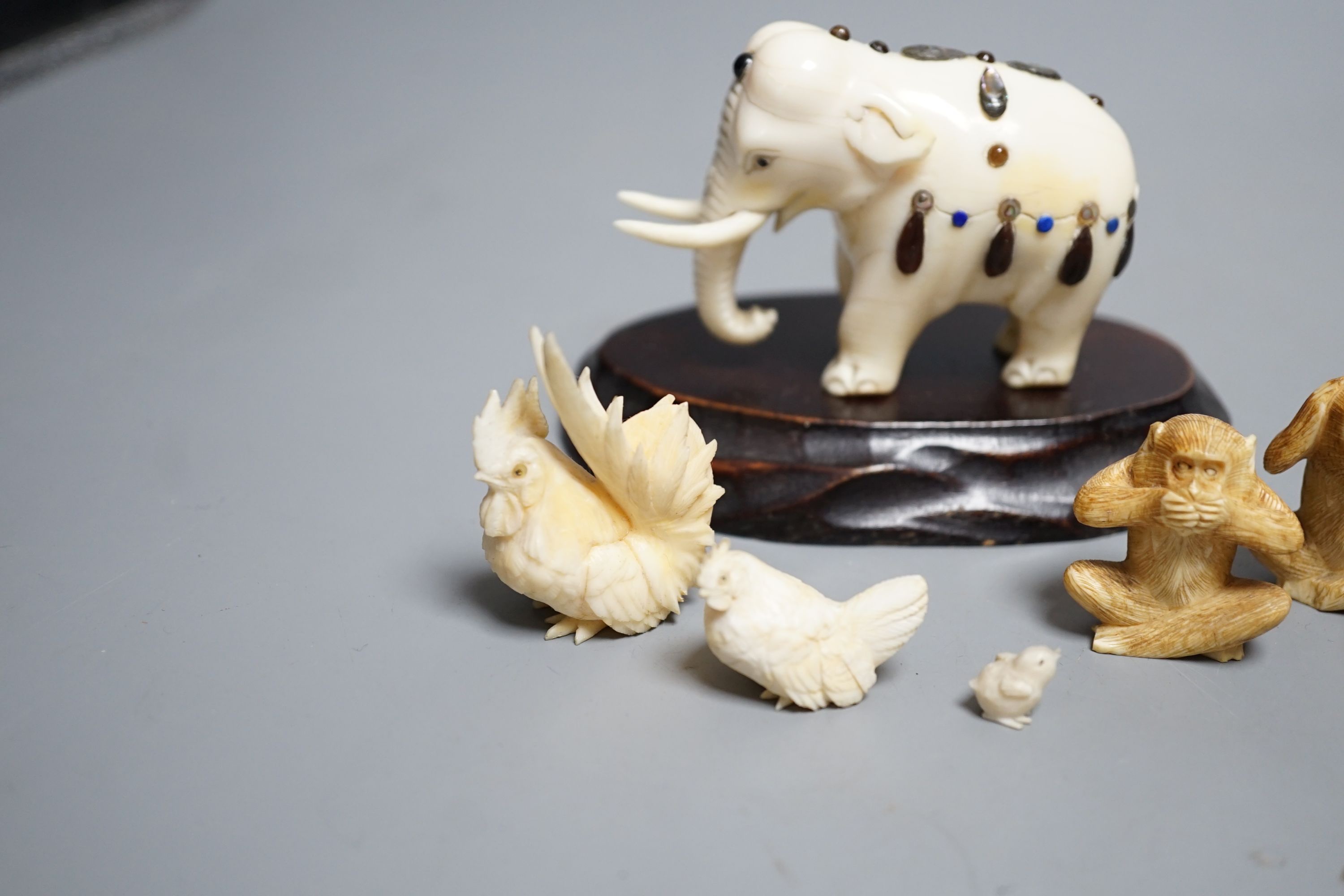 A Japanese Ivory and Shibayama style model of an elephant, three Japanese Ivory figures of the three wise monkeys and three Japanese ivory models of chickens and a chick, wood stand, all late 19th/early 20th century